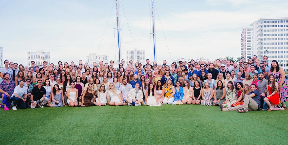 Chomps employees posing together on green artificial turf outdoors, with buildings and tall masts visible in the background under a pale sky.
